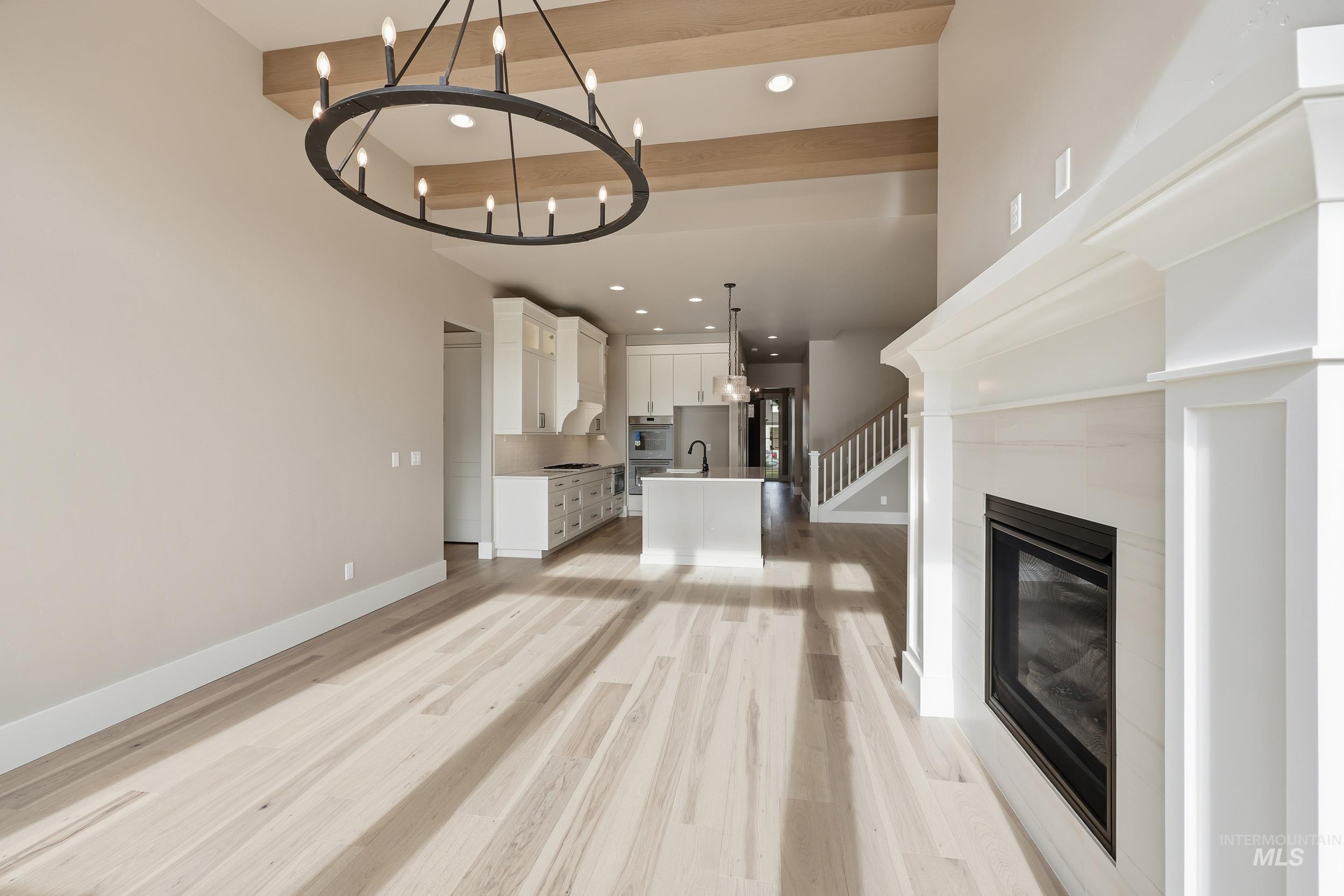 1035 East Crescendo Street Meridian, ID 83642 - Photo 3 of 50 Unfurnished living room with beam ceiling, stairs, recessed lighting, light wood-style floors, and a glass covered fireplace