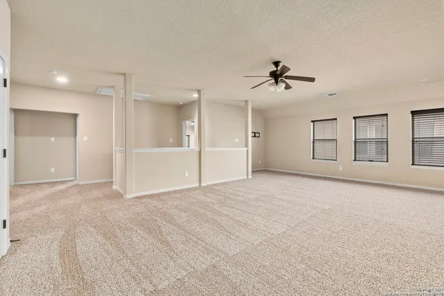 an empty room with chandelier fan and windows