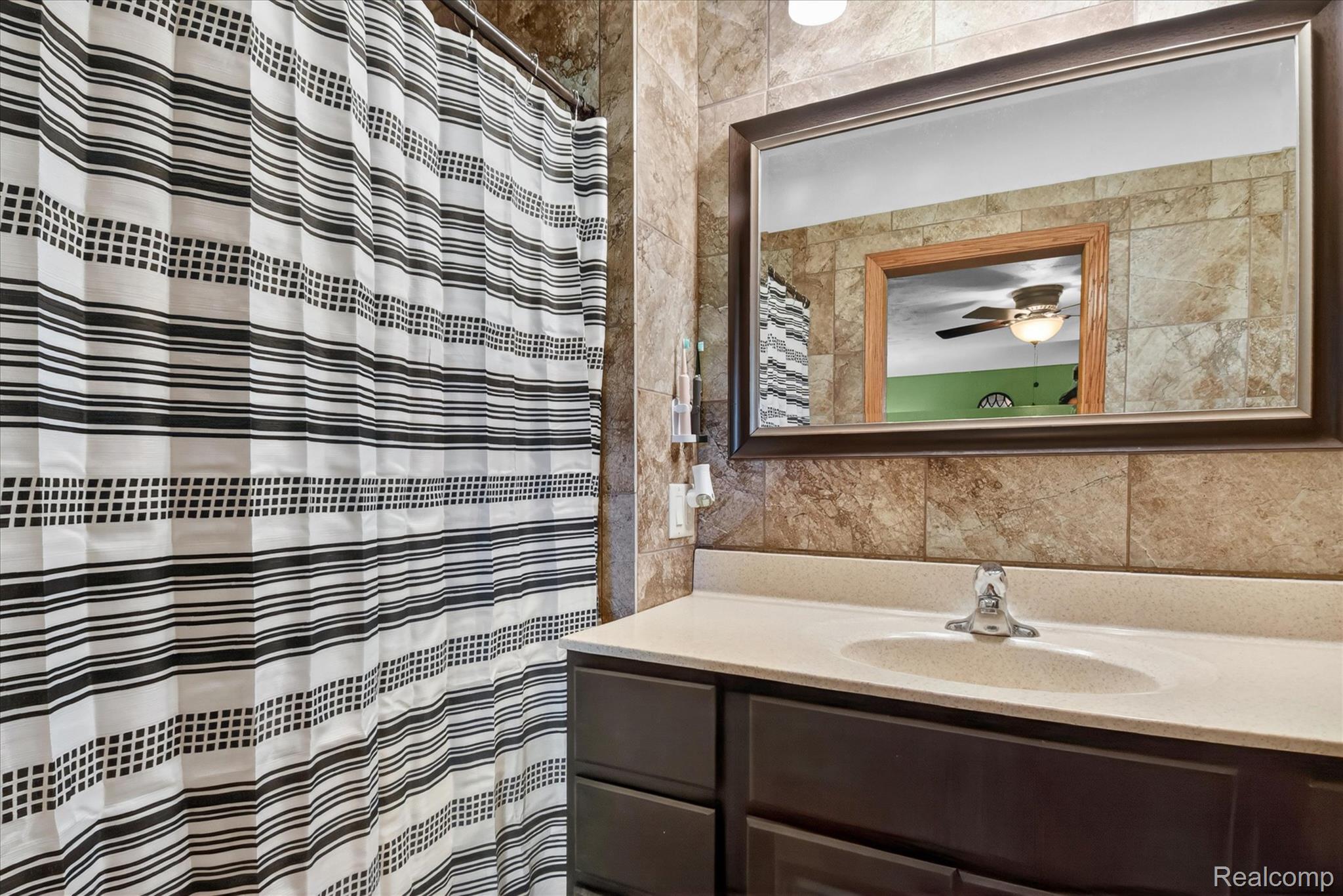 3949 West Burns Line Road Brown City, MI 48416 - Photo 29 of 70 Bathroom featuring a vanity with an integrated sink, a large framed mirror, and tile wall surround