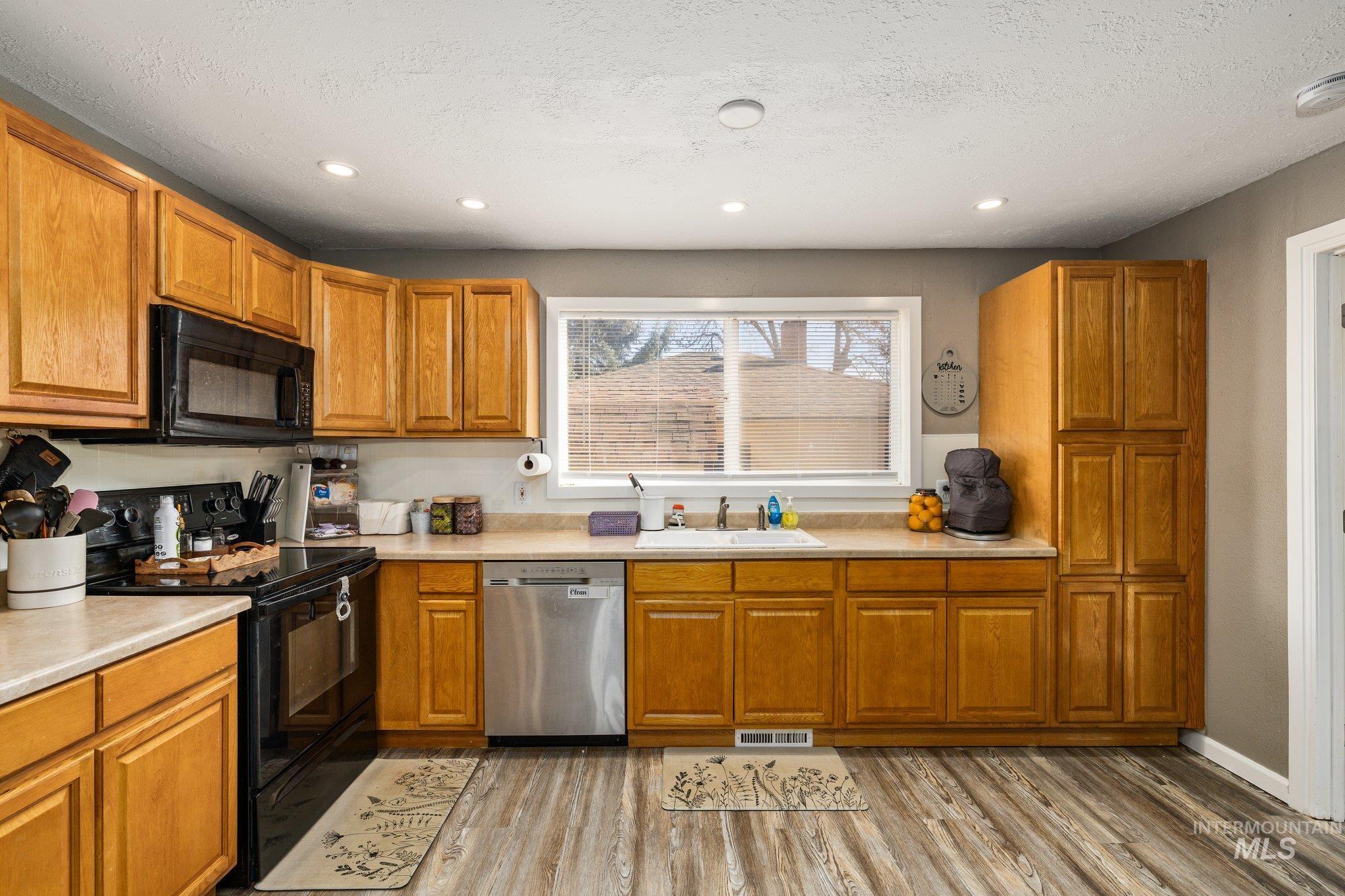 1504 2nd Street North Nampa, ID 83687 - Photo 12 of 29 Kitchen featuring black appliances, light countertops, wood finish cabinetry, light wood finished floors, and recessed lighting