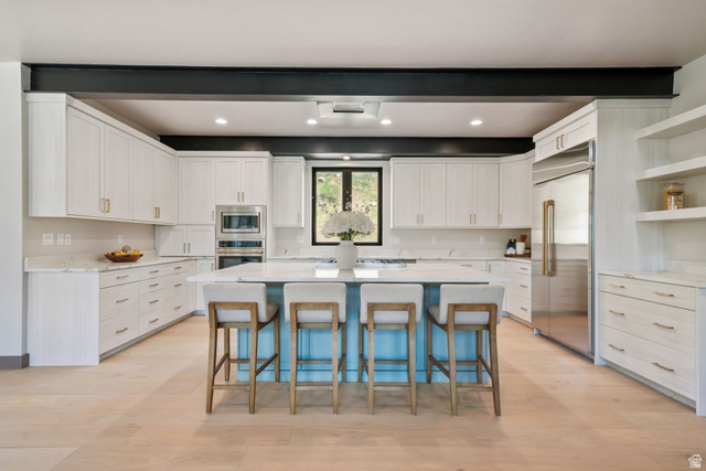 10646 North Reflection Ridge Hideout, UT 84036 - Photo 8 of 43 Contemporary kitchen featuring a light wood-finish floor, white cabinetry, integrated stainless steel appliances, and a central island with a light blue base and white countertop