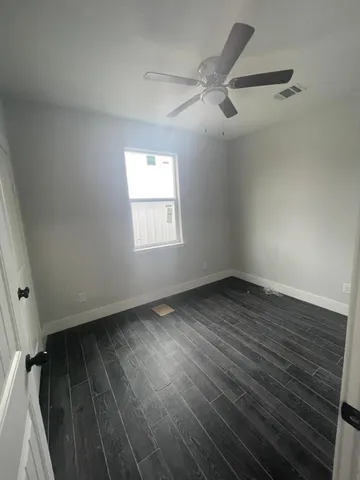 an empty room with wooden floor fan and windows
