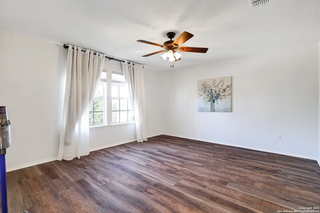 a view of empty room with wooden floor and fan