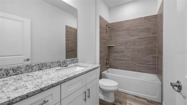 a bathroom with a granite countertop bathtub shower sink vanity and toilet
