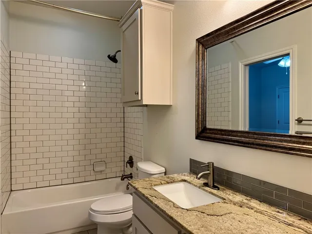 a bathroom with a granite countertop toilet a sink a mirror and bathtub