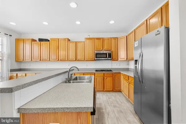 a kitchen with stainless steel appliances granite countertop a refrigerator a sink a stove with wooden cabinets and wooden floor