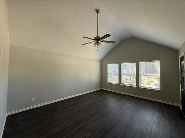an empty room with wooden floor fan and windows