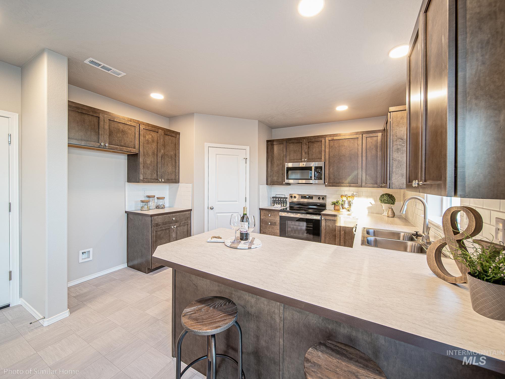 2049 Sumac Avenue Middleton, ID 83644 - Photo 3 of 6 Kitchen featuring light countertops, stainless steel appliances, decorative backsplash, dark brown cabinets, and recessed lighting