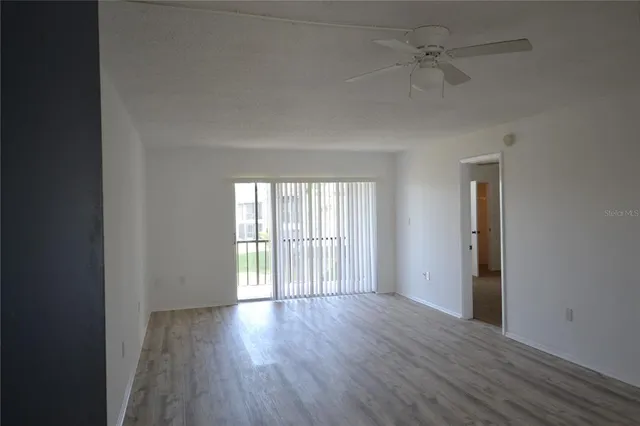 an empty room with wooden floor fan and windows