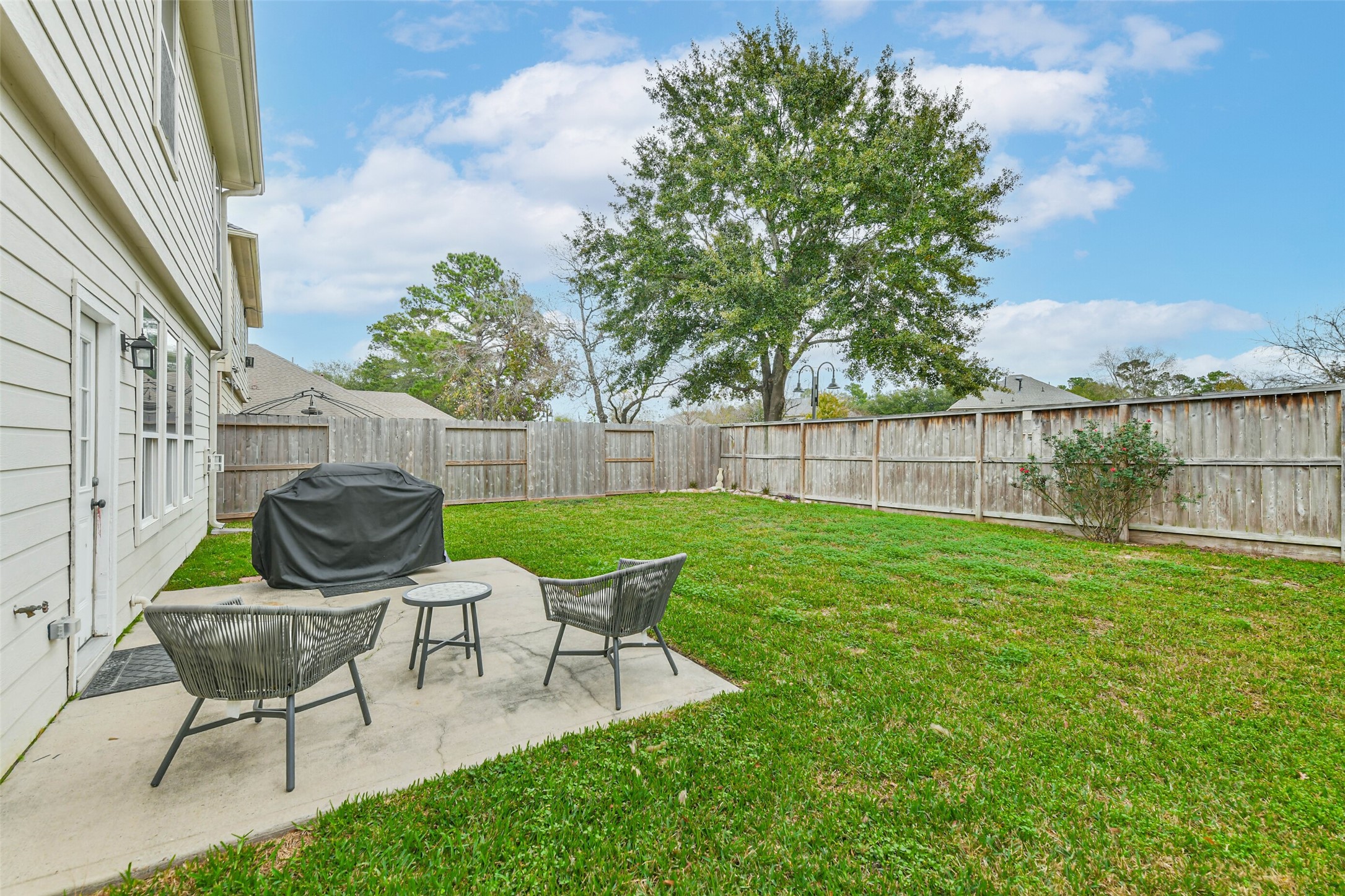 22538 Goss Spring Court Spring, TX 77373 - Photo 34 of 36 Spacious fenced backyard with a patio area featuring two chairs and a small table, perfect for outdoor relaxation. Includes a covered grill and a large tree providing shade, ideal for entertaining.