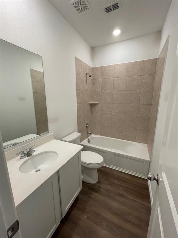 3700 Milkweed Road McKinney, TX 75071 - Photo 5 of 18 Bathroom featuring a white vanity with an undermount sink and polished chrome faucet, wood-finish flooring, and a shower/tub combination with beige tile surround