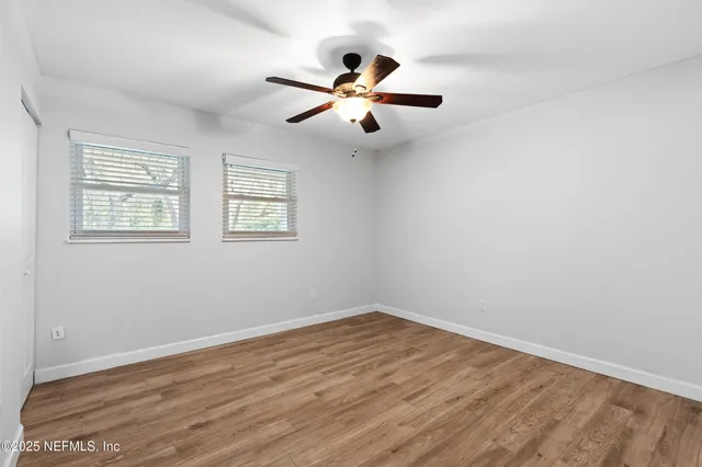 an empty room with wooden floor fan and windows