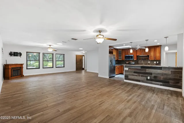 an empty room with wooden floor kitchen view and a window