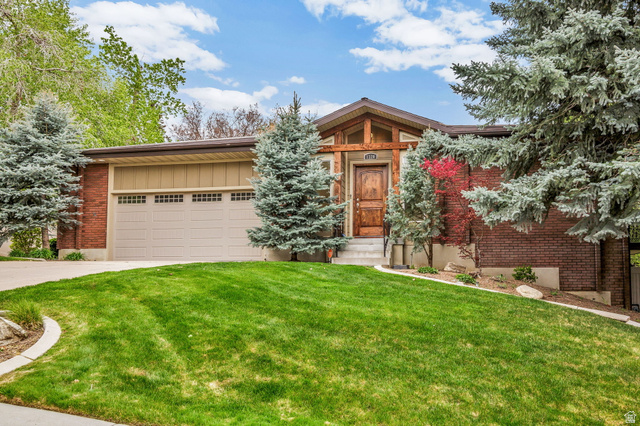 View of front of home with an attached garage, a front yard, driveway, entry steps, and brick siding