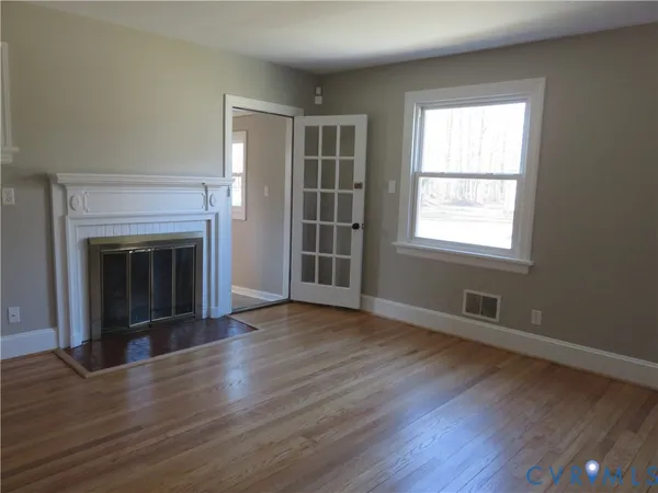 an empty room with wooden floor fireplace and windows