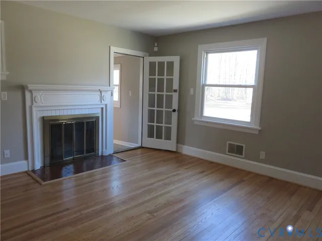 an empty room with wooden floor fireplace and windows
