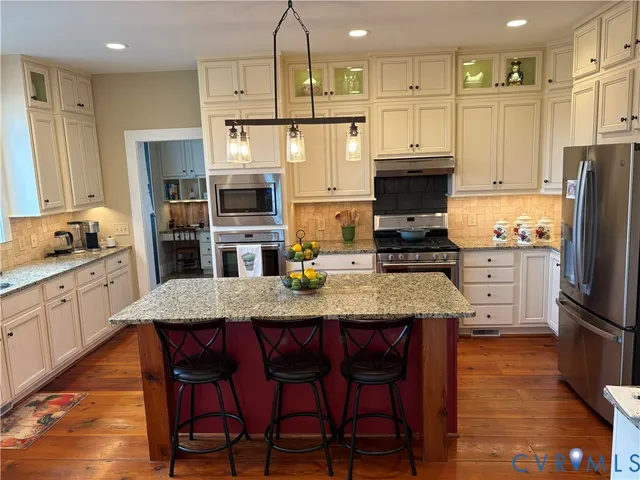 a kitchen with stainless steel appliances granite countertop a stove a refrigerator a sink a stove and white cabinets with wooden floor