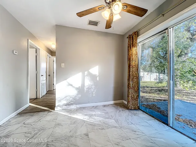 a view of an empty room with wooden floor and a ceiling fan
