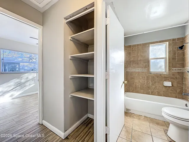 a view of an empty room with wooden floor and a ceiling fan