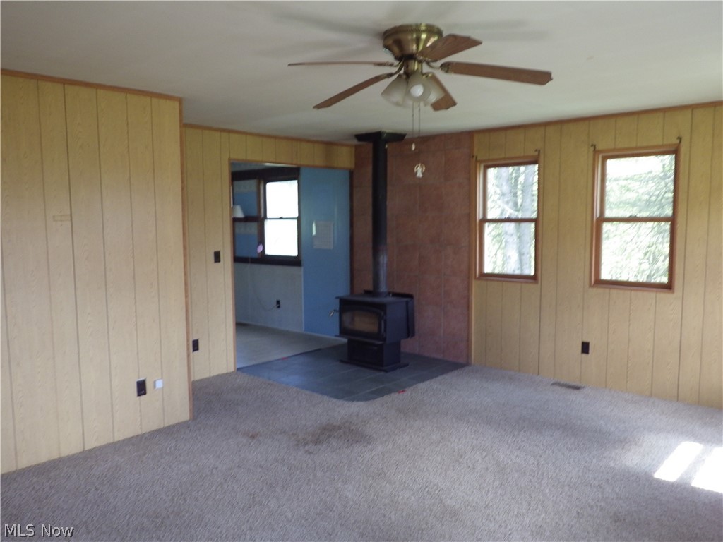 1446 Randolph Road Mogadore, OH 44260 - Photo 6 of 14 Unfurnished living room featuring a wood stove, ceiling fan, carpet floors, and wooden walls