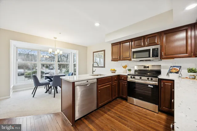 a kitchen with stainless steel appliances granite countertop a stove top oven a sink dishwasher a dining table and chairs with wooden floor