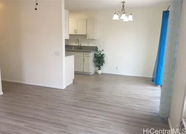 an empty room with wooden floor and kitchen view