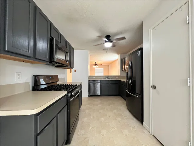 a kitchen with stainless steel appliances granite countertop a sink a stove top oven a refrigerator with grey cabinets