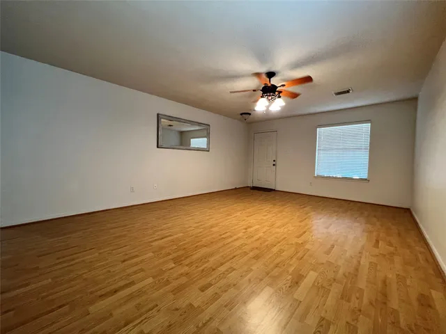 a view of an empty room with chandelier fan and wooden floor