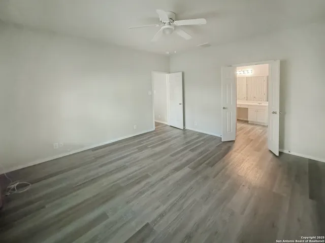 an empty room with wooden floor ceiling fan and windows