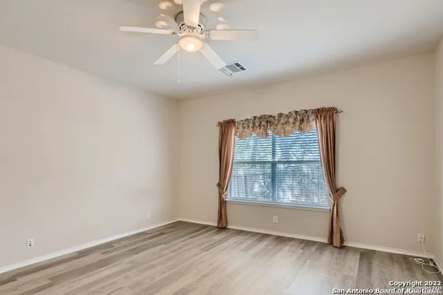 an empty room with wooden floor chandelier fan and windows