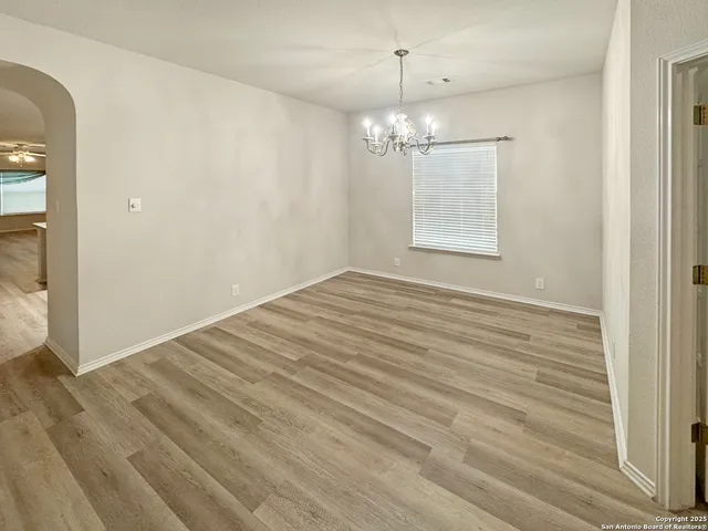 an empty room with wooden floor chandelier and windows