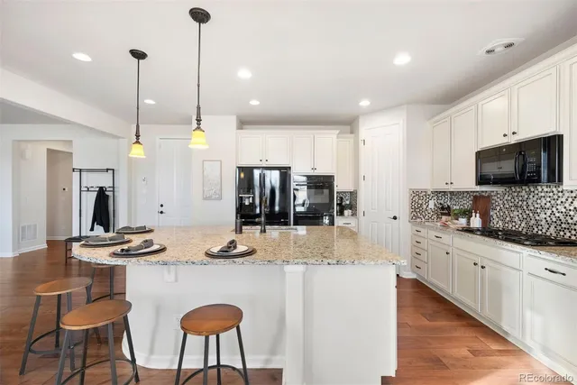a kitchen with stainless steel appliances kitchen island granite countertop a sink a stove a refrigerator and chairs