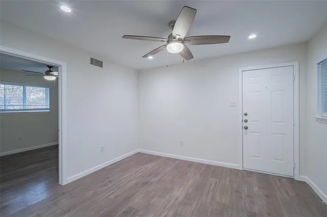 an empty room with wooden floor fan and windows