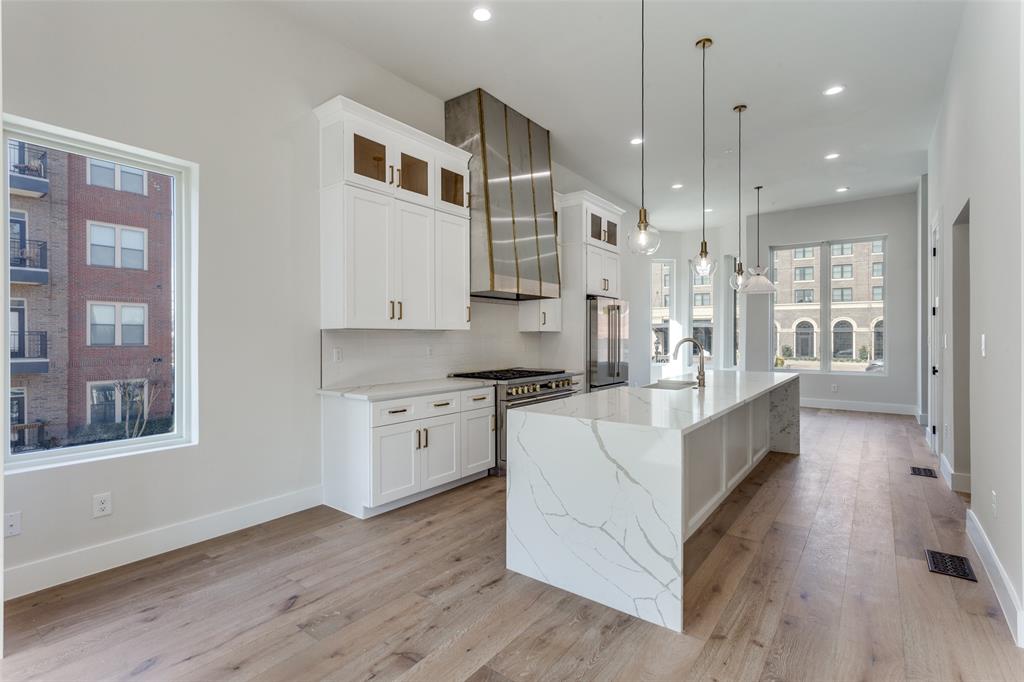 250 East Dallas Road, Unit 114 Grapevine, TX 76051 - Photo 12 of 33 a large white kitchen with kitchen island granite countertop a stove a sink a refrigerator and white cabinets with wooden floor