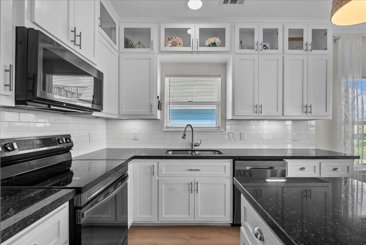 130 Beachcomber Avenue Surfside Beach, TX 77541 - Photo 12 of 33 This kitchen features modern countertops, white cabinetry with glass accents, a built-in microwave, and a sleek electric stove. It has a central sink under a window, providing natural light, with a bright, clean, and inviting atmosphere.