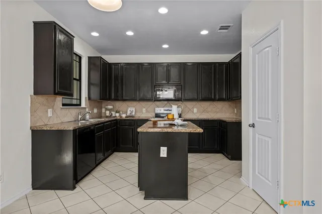 a kitchen with kitchen island granite countertop a refrigerator and a stove top oven