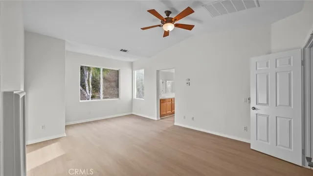 an empty room with wooden floor ceiling fan and windows