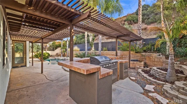 a view of a patio with a table and chairs under an umbrella with a barbeque