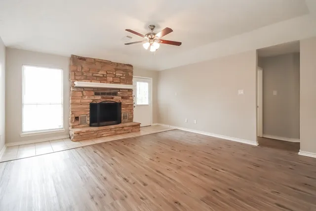 an empty room with wooden floor fireplace and windows