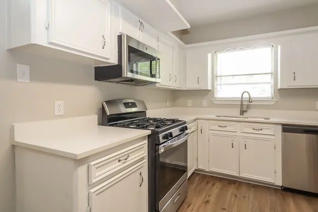 a kitchen with stainless steel appliances white cabinets granite counter tops and a window