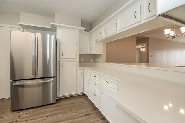 a kitchen with stainless steel appliances granite countertop a refrigerator a sink and white cabinets with wooden floor