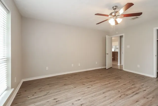 an empty room with wooden floor fan and windows