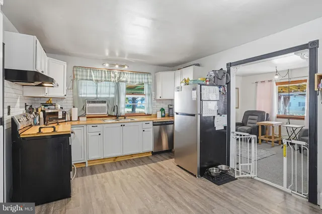 a kitchen with stainless steel appliances granite countertop a refrigerator a sink dishwasher a stove and white countertops with wooden floor