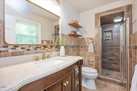 a bathroom with a granite countertop sink a toilet a mirror and shower