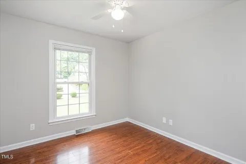 an empty room with wooden floor chandelier fan and windows