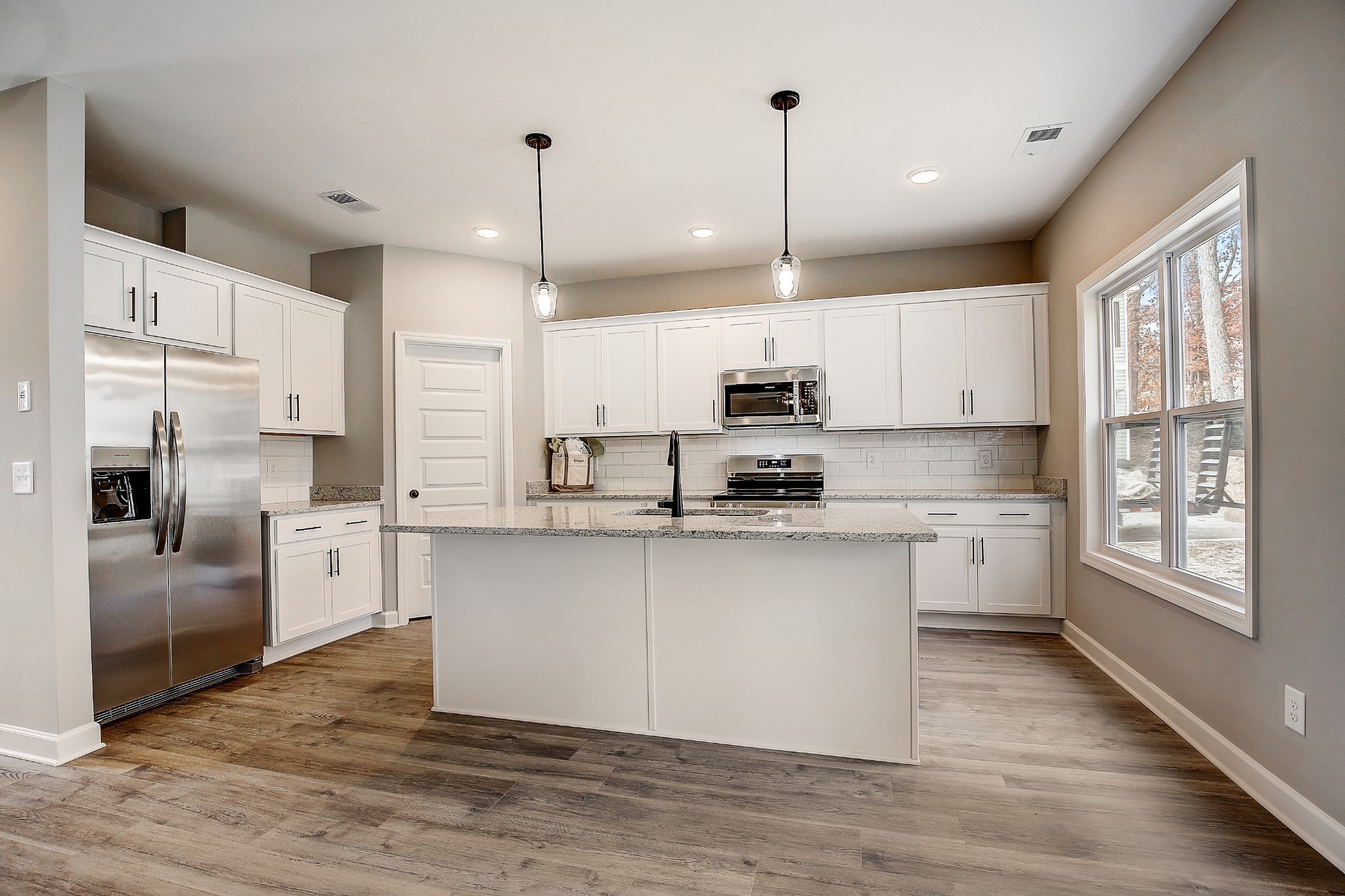 1770 Fenway Loop Antioch, TN 37013 - Photo 9 of 32 a large kitchen with white cabinets stainless steel appliances a large window and wooden floor
