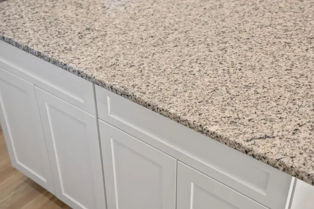 a close view of a sink a granite counter top a rug and a window