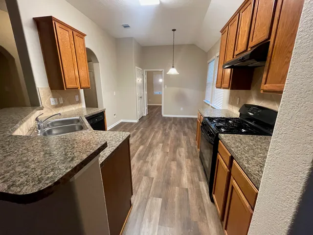 a kitchen with granite countertop a sink a stove and a wooden cabinets