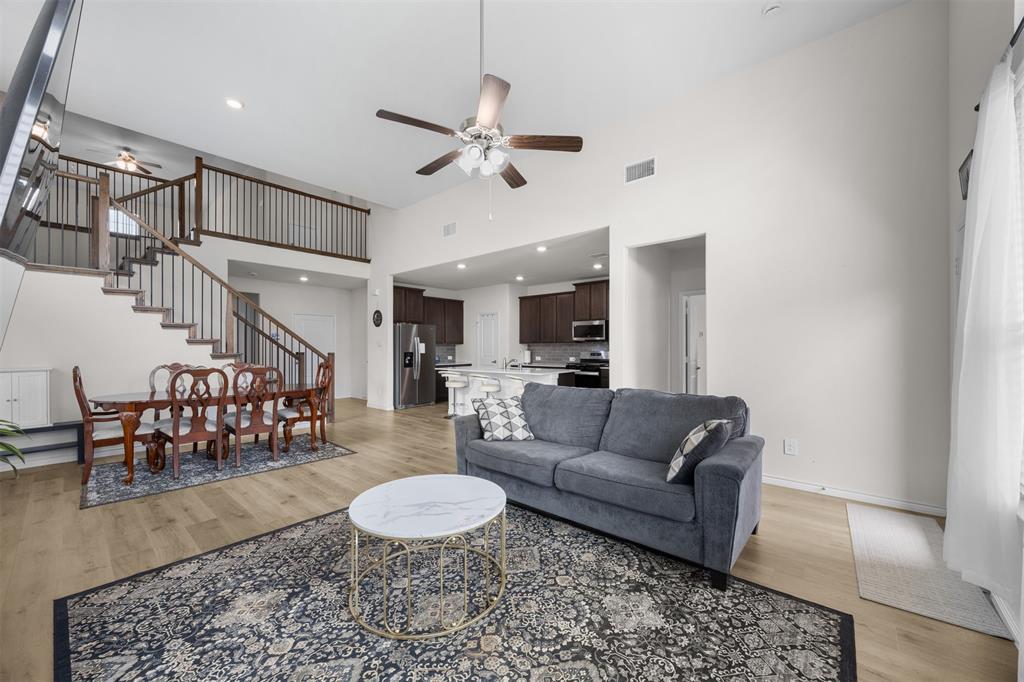 3808 High Country Road Aubrey, TX 76227 - Photo 7 of 36 Open-concept living area featuring high ceilings, wood-finish flooring, a contemporary staircase with dark wood railings and balusters, a kitchen with dark wood cabinetry and a white countertop island, and recessed lighting
