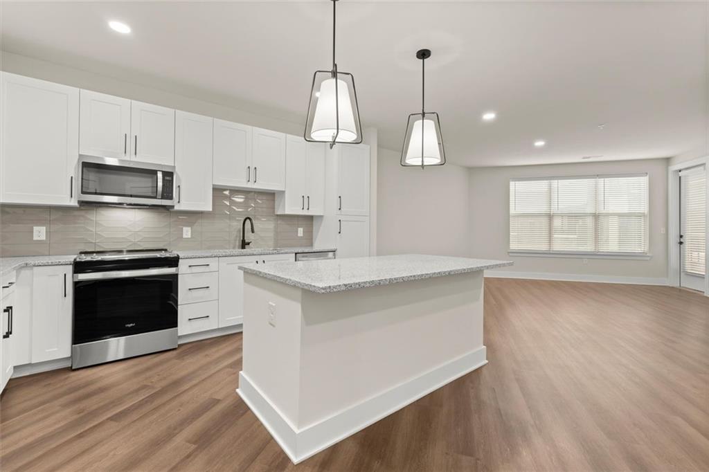 2648 Sandy Plains Road, Unit 422 Marietta, GA 30066 - Photo 3 of 37 a kitchen with kitchen island granite countertop a stove a sink and white cabinets with wooden floor
